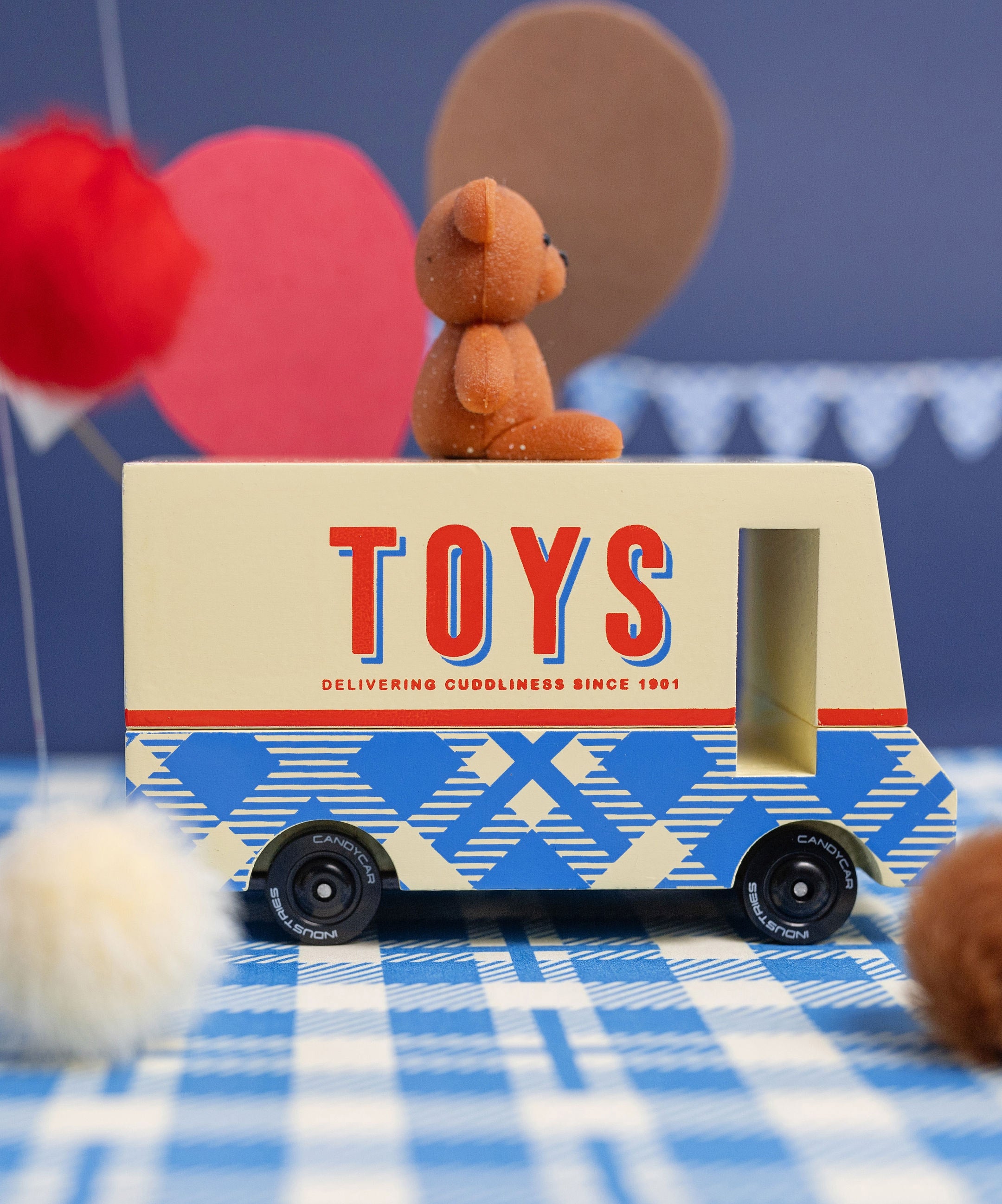 CandyLab cream and blue CandyVan with a brown teddy bear on the roof with Toys text logo in red on the side - on a blue checked cloth.