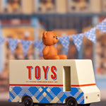 CandyLab cream and blue CandyVan with a brown teddy bear on the roof with Toys text logo in red on the side - with blue check bunting in the background.