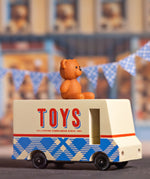 CandyLab cream and blue CandyVan with a brown teddy bear on the roof with Toys text logo in red on the side - with blue check bunting in the background.