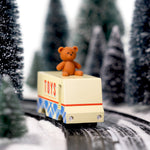 CandyLab cream and blue CandyVan with a brown teddy bear on the roof with Toys text logo in red on the side - on a road going through a snowy forest.