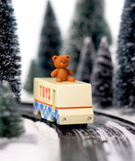 CandyLab cream and blue CandyVan with a brown teddy bear on the roof with Toys text logo in red on the side - on a road going through a snowy forest.