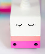 A side view of The Candyvan Unicorn 2.0 Van with colourful stripes and a Unicorn horn topper behind its cardboard box