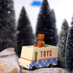CandyLab cream and blue CandyVan with a brown teddy bear on the roof with Toys text logo in red on the side - parked on rocks with a snowy forest in the background.