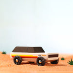 Candylab children's handmade wooden Wanderer car toy on some sand on a light blue background