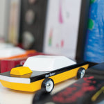 Candylab plastic-free yellow and black car toy on a shelf next to other Candylab toy cars and some children's drawings