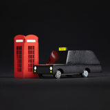 Candylab wooden London taxi car toy on a white snow scene background next to some miniature trees and red phonebox