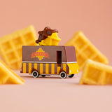 Candylab toy waffle truck on a pink background next to pieces of waffle