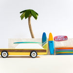 Candylab collectable yellow woodie car toy on a sandy background in front of some miniature surfboards and palm tree
