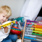 Young child holding a Candylab wooden taxi cab toy next to a rainbow wooden abacus