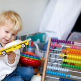 Young child holding a Candylab wooden taxi cab toy next to a rainbow wooden abacus