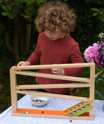 A child playing with the Beck Toys Chimes Marble Run Track. The beech wood track has four wooden ramp tracks and glockenspiel note steps to finish. 