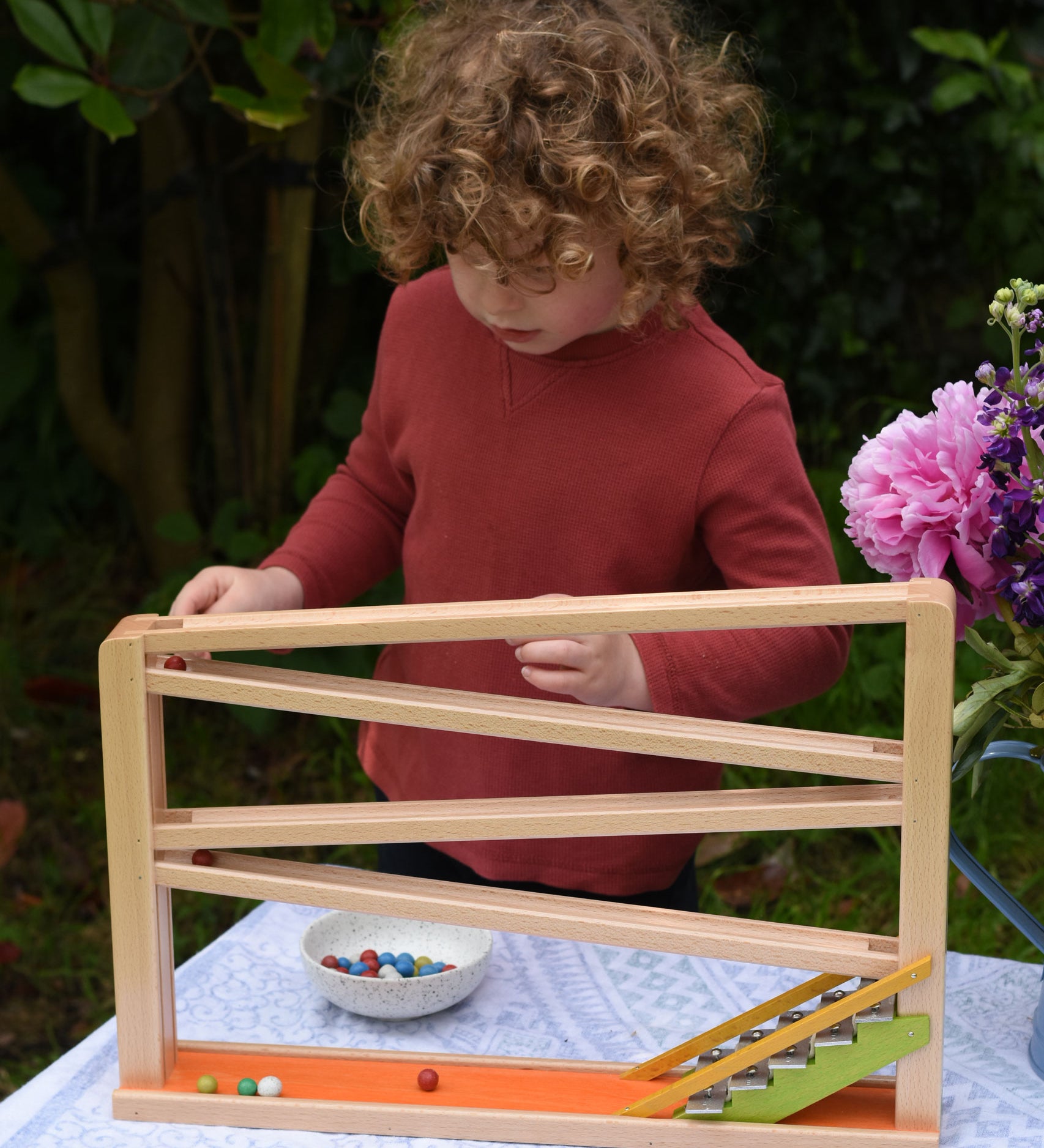 A child playing with the Beck Toys Chimes Marble Run Track. The beech wood track has four wooden ramp tracks and glockenspiel note steps to finish. 