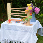 A collection of Beck Spielwaren wooden toys placed on a small table outdoors. The Wobbler tumbling toy, the run plate chimes marble run tower and the chimes marble run track. 