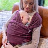 Mother carrying a baby in Close Caboo cotton blend soft structure Baby Carrier in burgundy showing wide shoulder straps and soft front panel