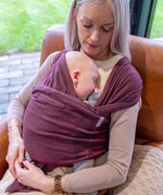 Mother carrying a baby in Close Caboo cotton blend soft structure Baby Carrier in burgundy showing wide shoulder straps and soft front panel