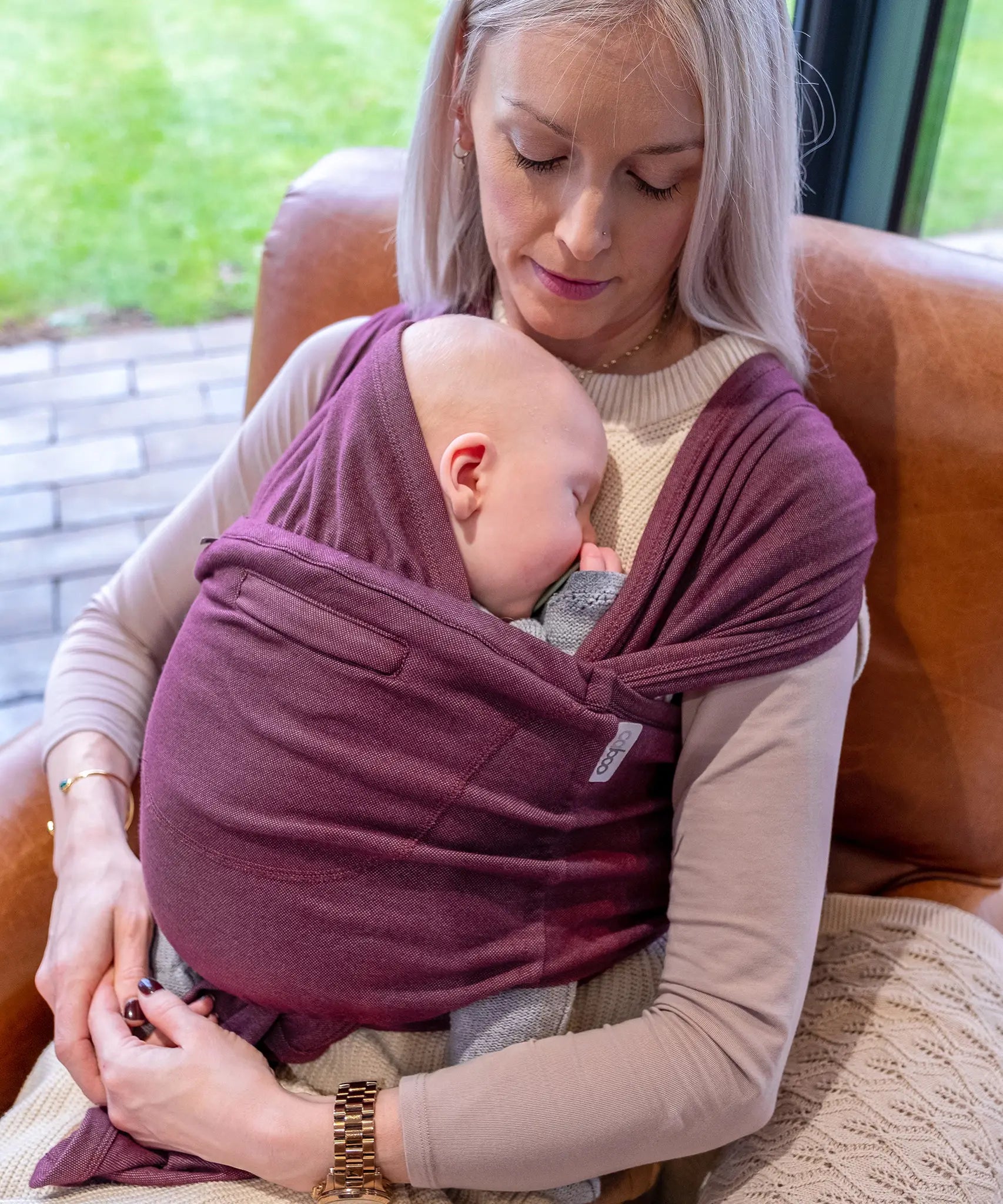 Mother carrying a baby in Close Caboo cotton blend soft structure Baby Carrier in burgundy showing wide shoulder straps and soft front panel