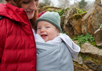 Close Caboo Lite Baby Carrier in Alloy shown outdoors with a smiling baby carried close against the wearer’s chest.