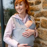 Woman babywearing with the Close Caboo Lite Baby Carrier in Alloy worn in front carry, showing a sleeping newborn supported close to the her.