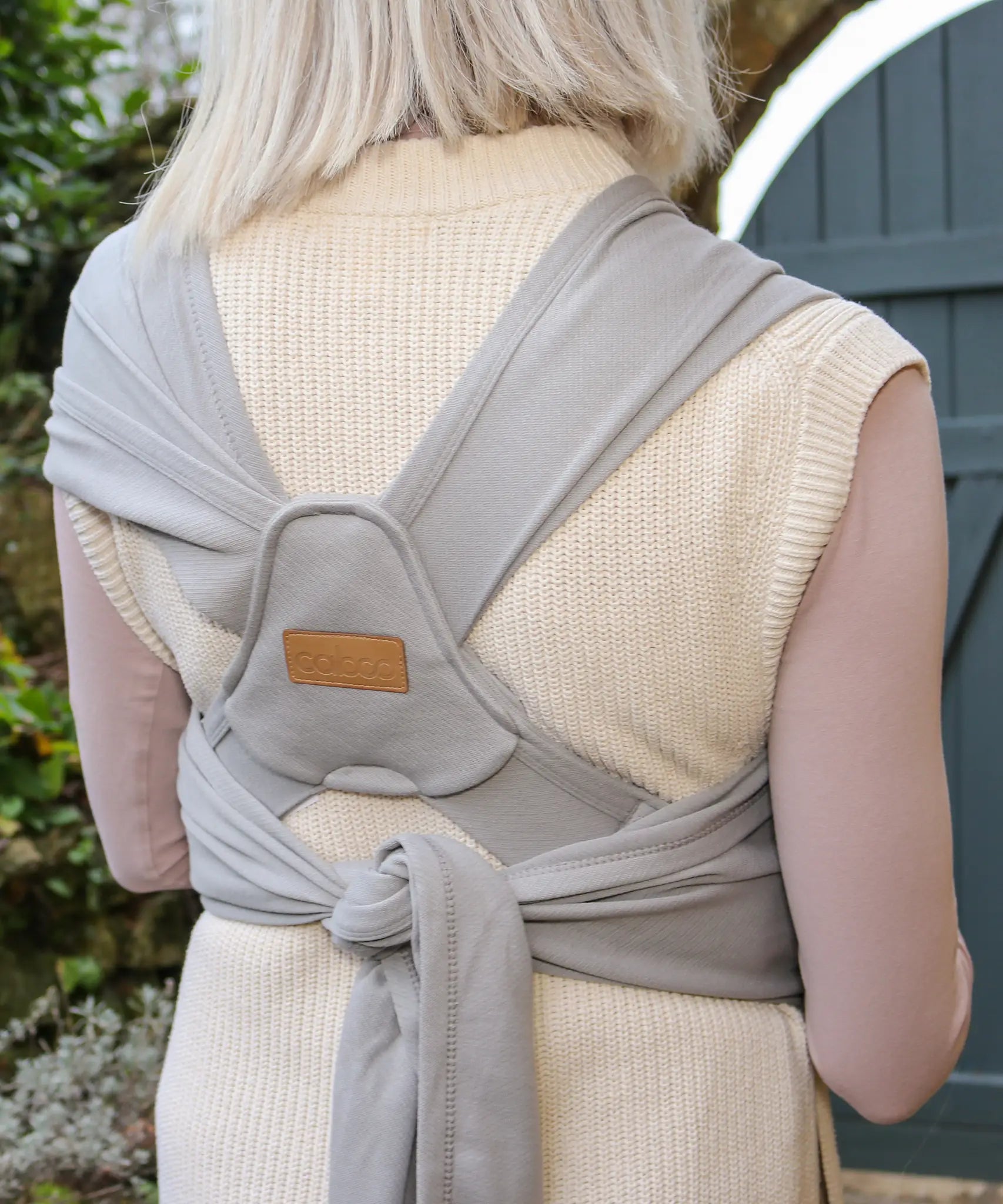Back of woman wearing a Close Caboo Organic Baby Carrier in porpoise  showing wide shoulder straps, tie waist strap, and soft supportive panel.
