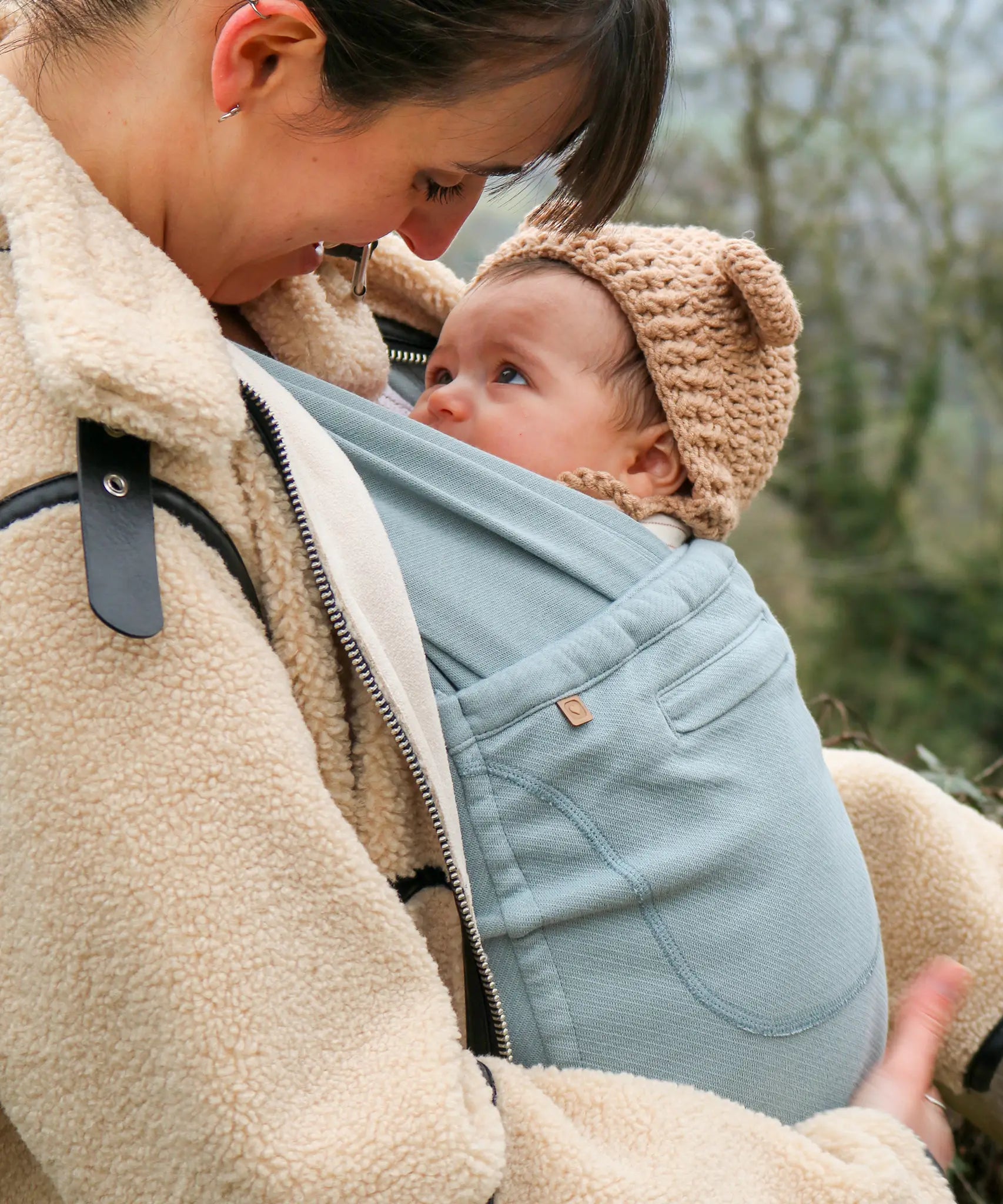 Side of mother carrier a baby in a Close Caboo Organic Baby soft structure cotton Carrier in sage