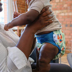 A little baby wearing The Close Parent Pop-in reusable nappy wrap cover with velcro closures, in an orangutan print