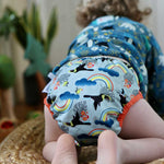 A baby wearing The Close Pop-In +bamboo reusable cloth nappy with adjustable popper closures, in a toucan print
