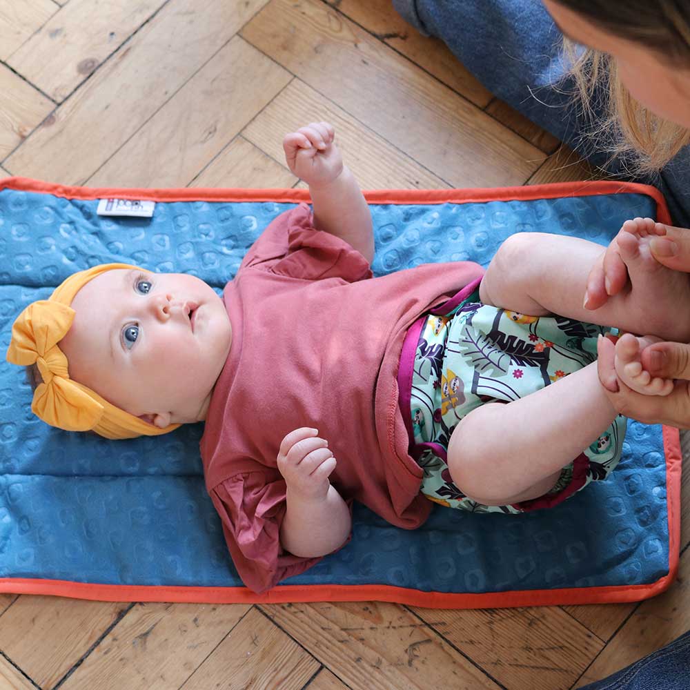 A little baby wearing The Close Parent Pop-in reusable nappy wrap cover with velcro closures, in a sloth print