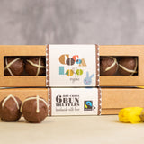 Boxes of Cocoa Loco eco-friendly hot cross bun chocolate easter truffles stacked on a table next to some yellow easter eggs
