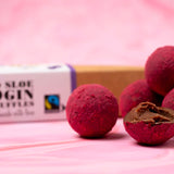 Close up of a pile of Cocoa Loco fairtrade milk chocolate gin truffles on a pink background next to their cardboard box