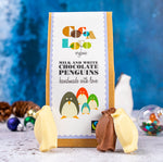 3 Cocoa Loco organic white and milk chocolate penguins leaning against their box on a blue and white Christmas background