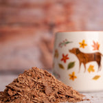 Close up of a pile of Cocoa Loco organic hot chocolate flakes in front of an orange and white mug