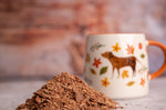 Close up of a pile of Cocoa Loco organic hot chocolate flakes in front of an orange and white mug