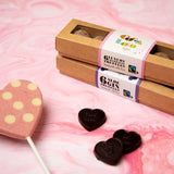 Cocoa Loco champagne truffles box next to a pink heart lollipop and some dark chocolate hearts on a pink background