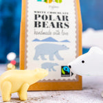 Close up of a Cocoa Loco white chocolate polar bear next to a wooden toy polar bear in front of its cardboard box