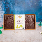 Cocoa Loco organic, fair-trade, christmas milk chocolate slab on a blue Christmas scene background and cream table. Chocolate slab has images of woodland stags, trees and leaves indented into it.