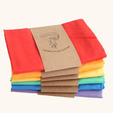 Six organic cotton play cloths by Laura's Play Cotton, in solid colours folded and stacked in rainbow order.