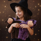 A child wearing a witches hat cuddling two Olli Ella cozy dozy bats in brown and purple. These soft toys are part of Olli Ella's Halloween collection available here at Babipur. 