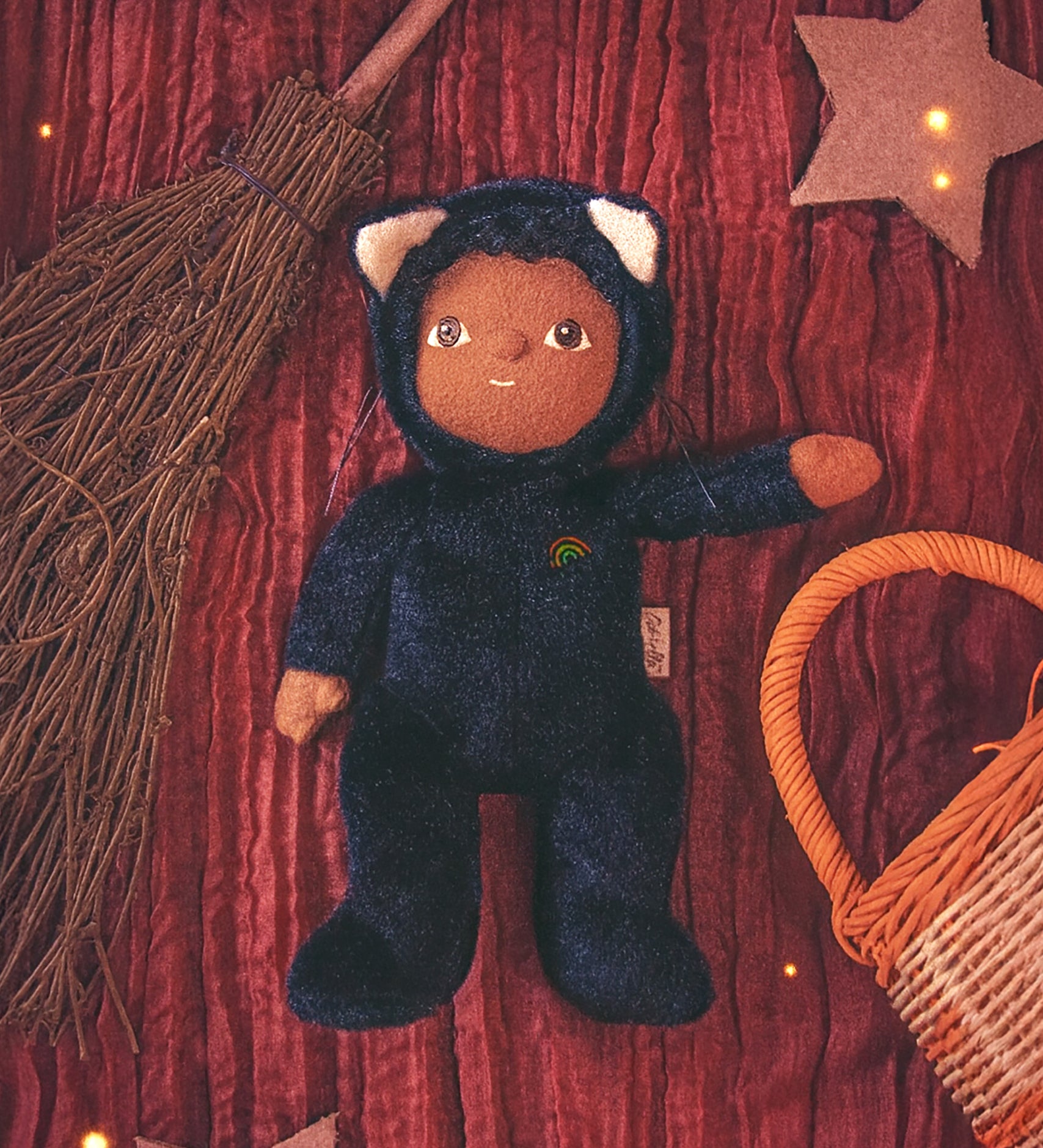 Olli Ella Carson Cat Dinky Dinkum Doll. This soft toy is a black cat with glow in the dark inner ears and a small embroidered rainbow detail on the chest. The cat has been placed in the middle of a Halloween themed flatlay. These soft toys are part of Olli Ella's Halloween collection available here at Babipur.