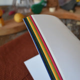 Kite paper squares for crafting. Book of 100 22cm square sheets in various colours. View of side of sheets.