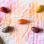 Close up of some coloured Crayon Rocks on top of a leaf rubbing on some white paper