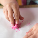 Close up of a child drawing with a pink Crayon Rock on some white paper