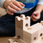 Close up of a child holding a green glass marble above a set of stacking Cuboro wooden marble run toy blocks