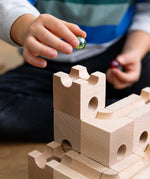 Close up of a child holding a green glass marble above a set of stacking Cuboro wooden marble run toy blocks