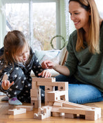 Child and adult sat on a wooden floor playing with the Cuboro handmade wooden marble run toy blocks