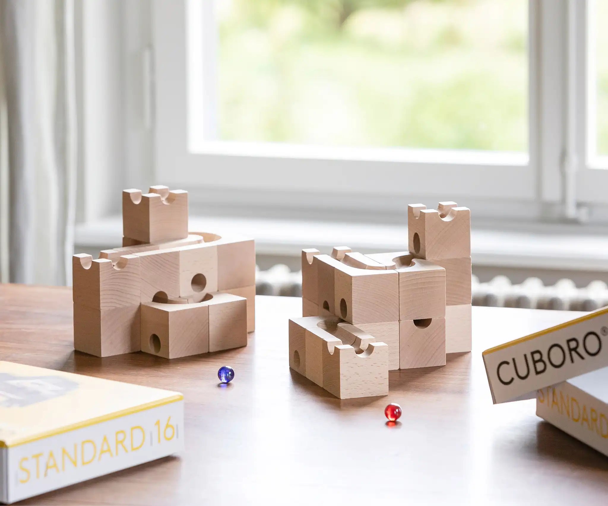 Cuboro standard 16 piece wooden marble run set up on a table with a blue and red glass marble placed besides them.