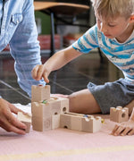 Cuboro standard 16 piece wooden marble run set played with by a child and an adult on the floor.