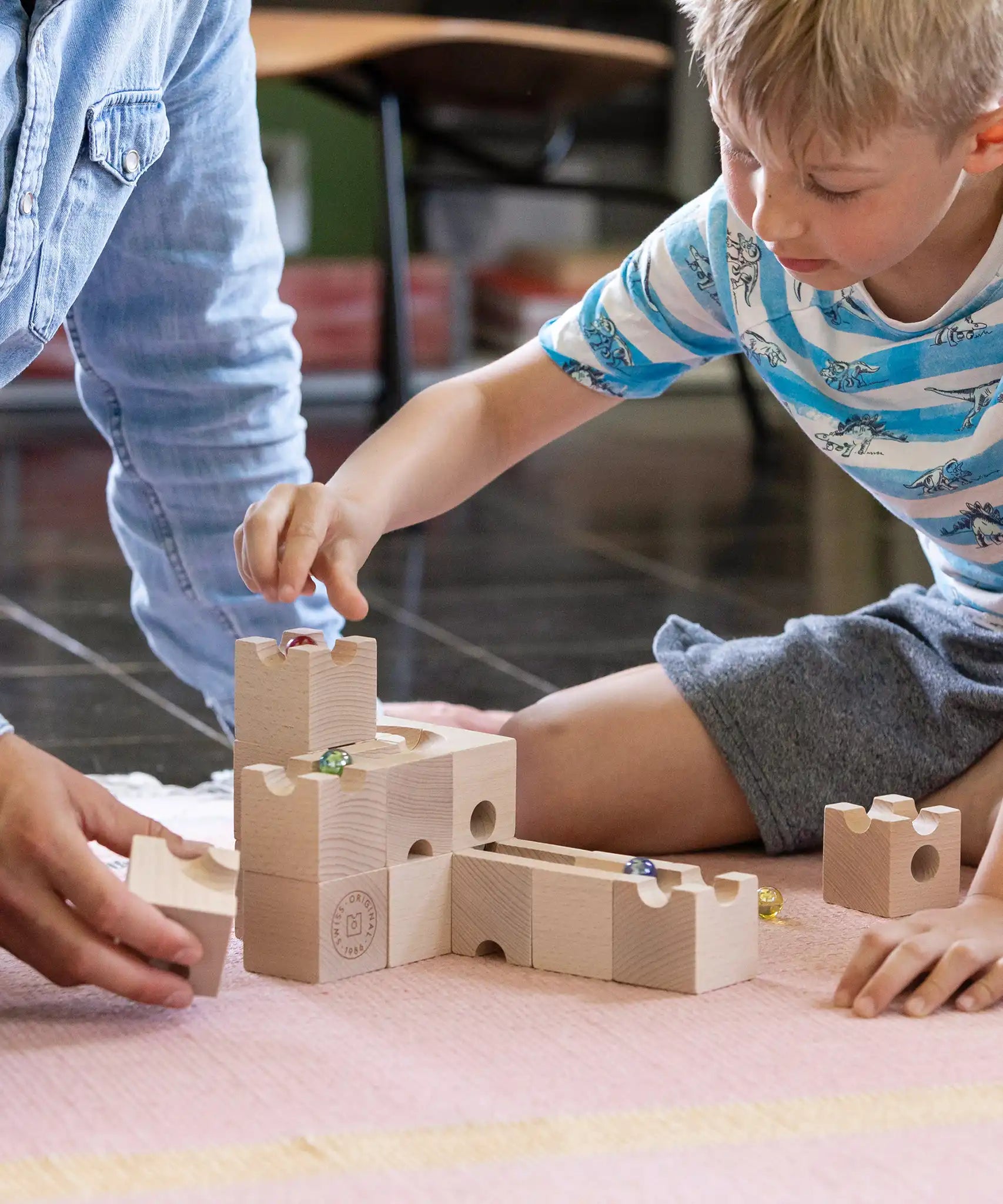 Cuboro standard 16 piece wooden marble run set played with by a child and an adult on the floor.