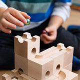 Cuboro Standard wooden marble run  32 piece set set up on the floor with a child placing a green glass marble in the starting point.