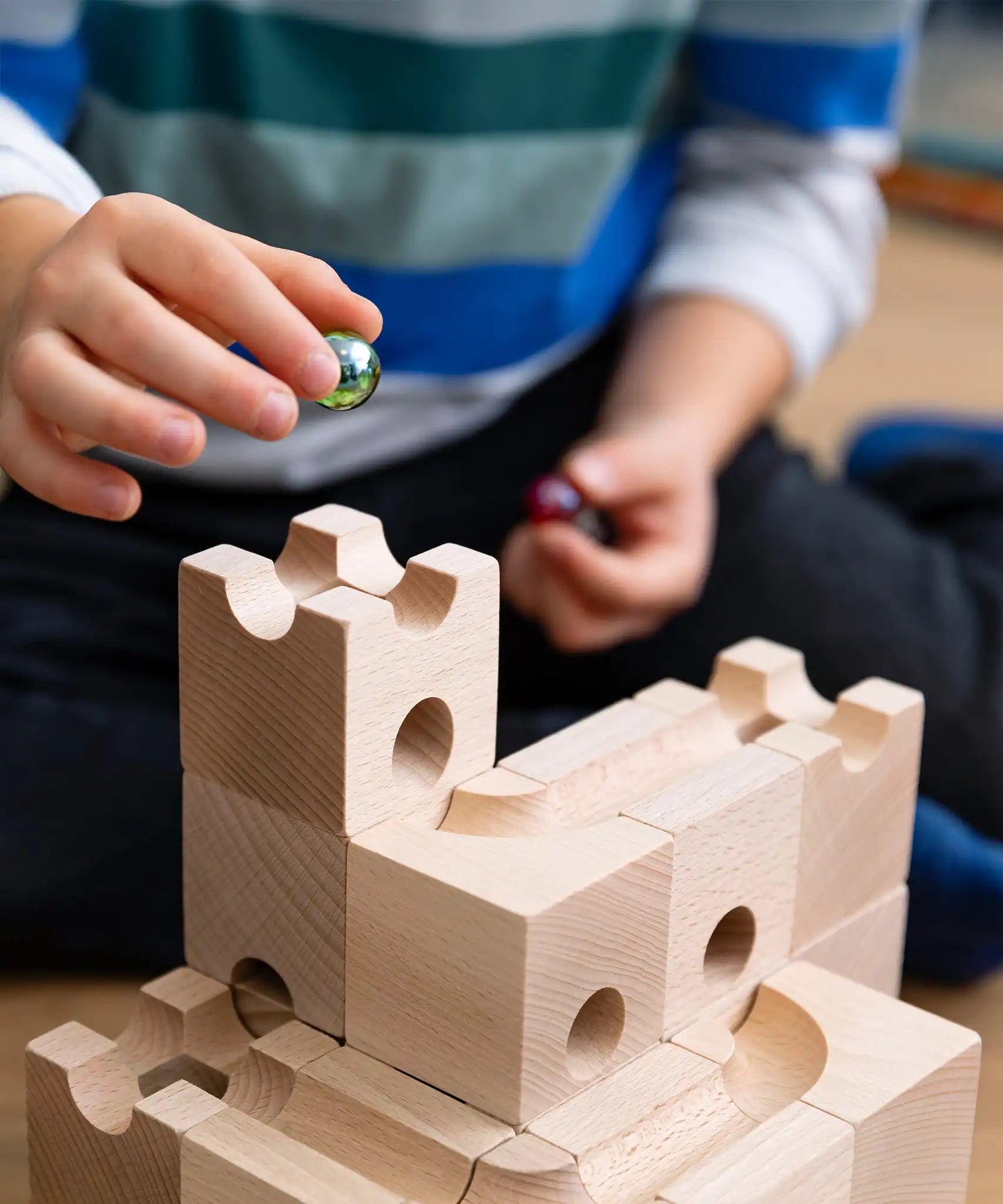 Cuboro Standard wooden marble run  32 piece set set up on the floor with a child placing a green glass marble in the starting point.