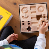 Cuboro standard 50 piece wooden marble run set in it's box, a child's hand can be seen taking a piece out of the box. 